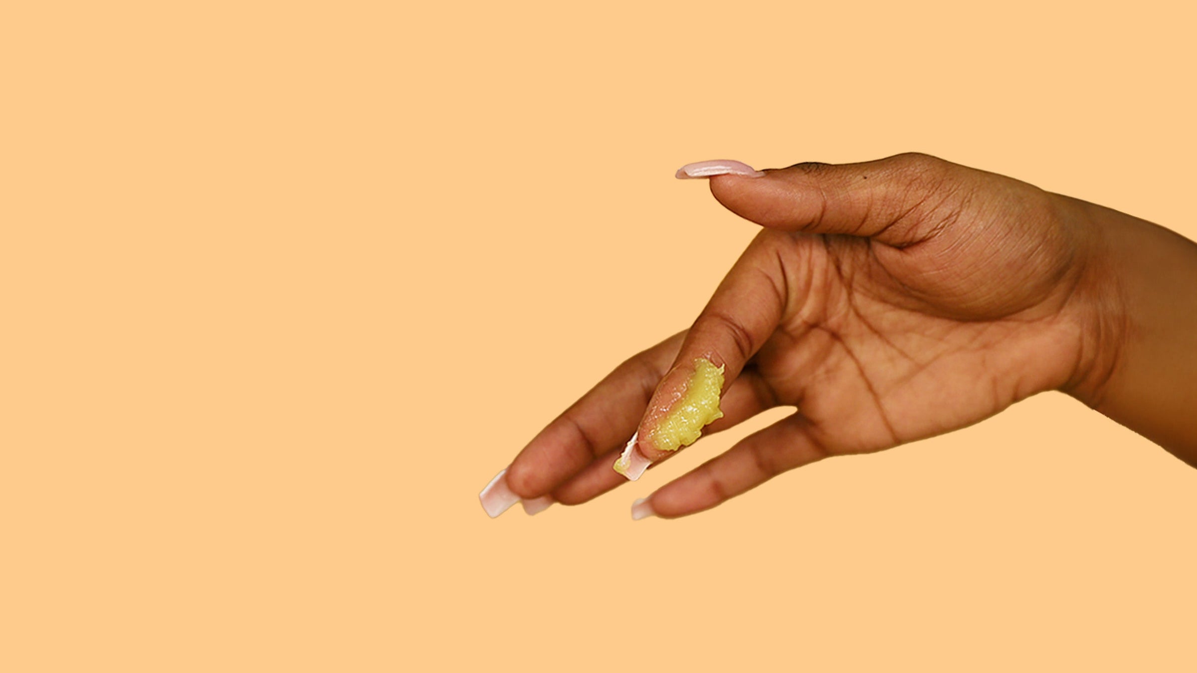 Hand with Herb’n Eden salve on finger on an orange background.